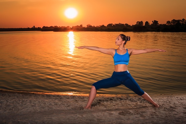 yoga bij zonsondergang op het strand. vrouw die yoga doet, asanas uitvoert en van het leven op de rivier geniet