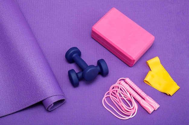 Yoga brick dumbbells jump rope fitness band on purple gym mat