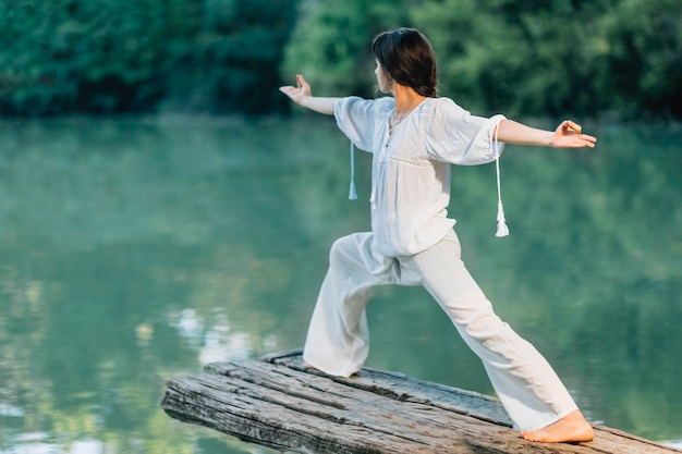 Photo yoga by the lake young woman practicing warrior 2 pose