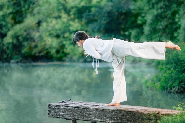 Foto yoga sul lago giovane donna che pratica il guerriero 3 pose o virabhadrasana iii