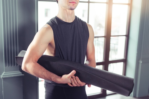 Yoga concept. Young men rolling mat after a yoga on black wooden floor