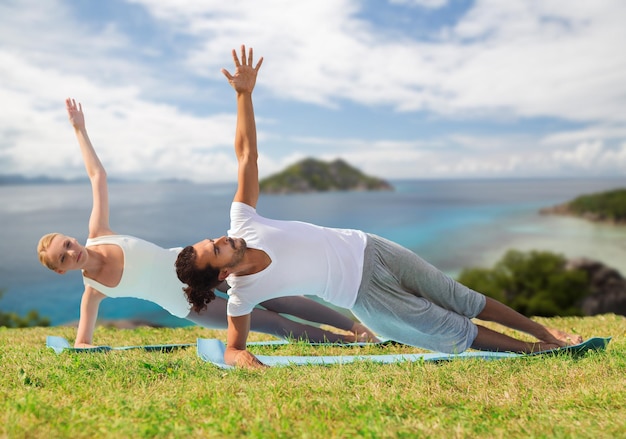 yoga, fitness, sport and people concept - couple doing plank exercise on mats outdoors