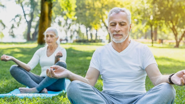 Foto yoga in het park senior koppel zittend in lotushouding op groen gras in rust en meditatie