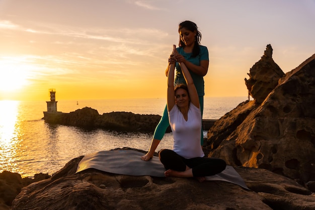 Инструктор по йоге, работающий со студентом на природе у моря на закате, здоровая и натуристская жизнь, пилатес на открытом воздухе