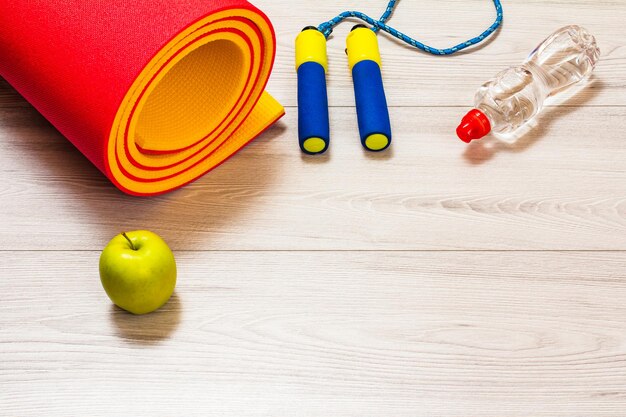 Yoga mat and different tools for fitness on floor in room.