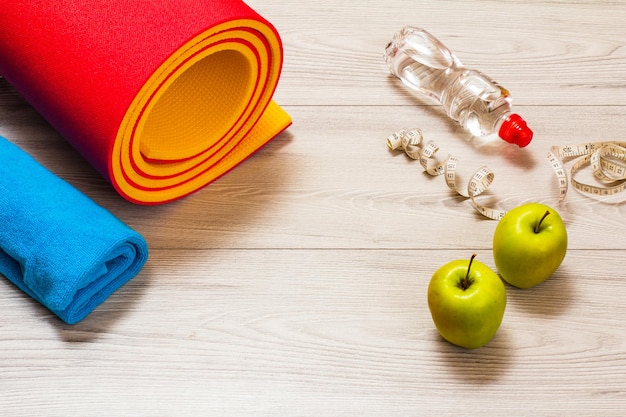 Yoga mat and different tools for fitness on floor in room.