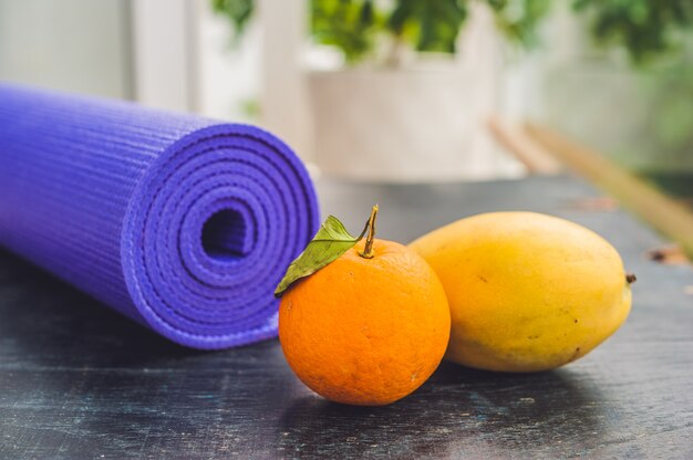 Yoga mat, orange and mango on a wooden background