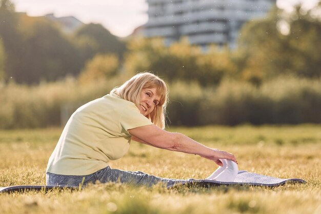 On yoga mat senior woman having nice weekend outdoors on the
field at sunny day