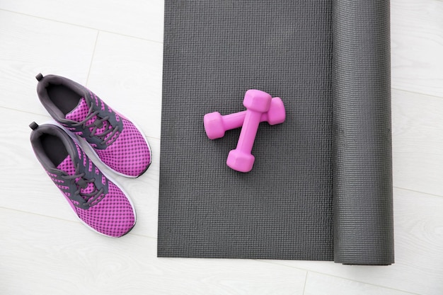 Yoga mat sneakers and dumbbells on light background