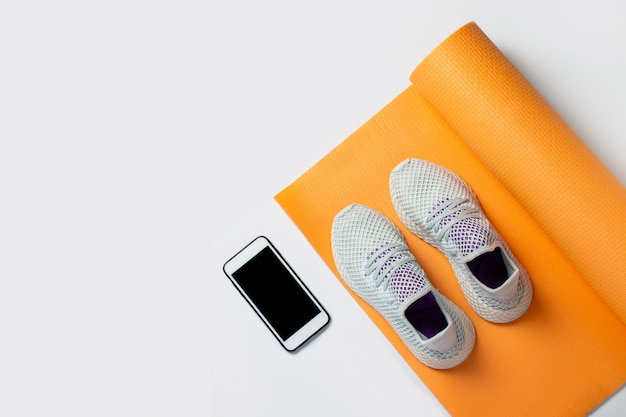 Yoga mat, sneakers and phone on a white background. Sports, yoga and training. Top view