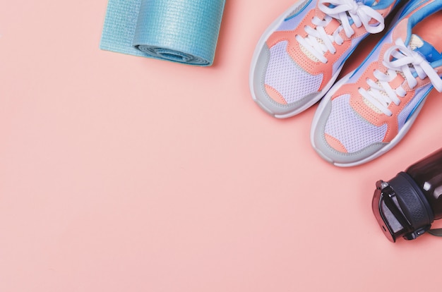 Yoga mat, sport shoes, bottle of water on pink