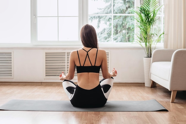 Yoga e meditazione a casa ragazza seduta su una stuoia e meditando vista posteriore