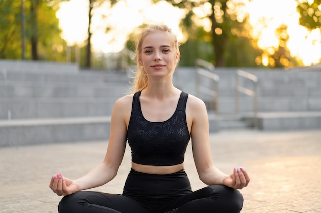 Yoga e meditazione in città moderna donna caucasica rilassarsi posizione del loto seduta tappetino yoga all'aperto parco estivo su pavimento di cemento giovane adulto femmina in forma rilassante dopo l'allenamento pratica yoga siddhasana