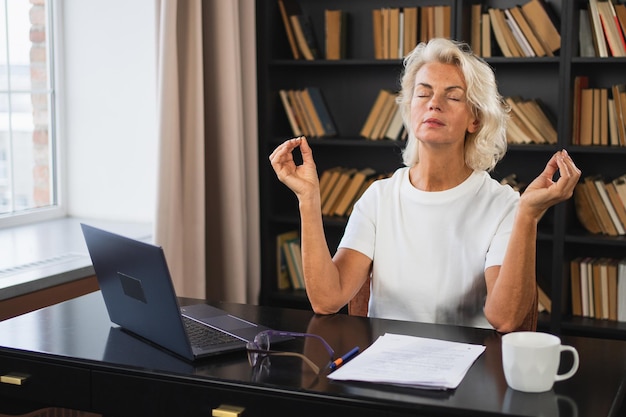 Yoga, mindfulness, meditatie, geen stress, kalm blijven. Een vrouw van middelbare leeftijd die yoga beoefent op kantoor.