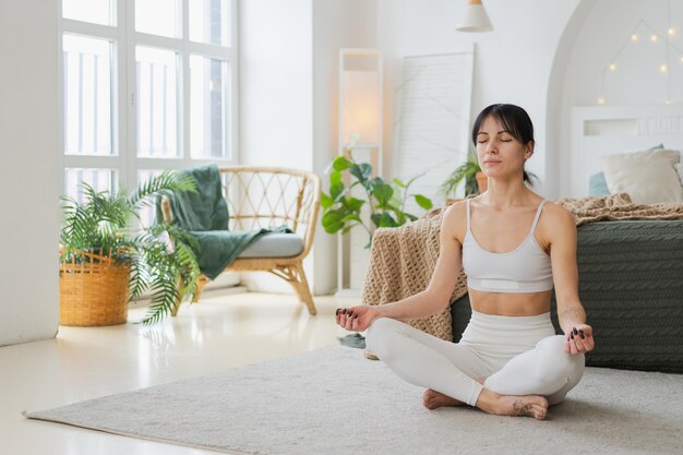 Foto yoga mindfulness meditazione giovane donna sana che pratica yoga nel soggiorno a casa donna seduta