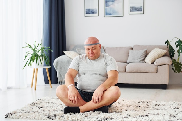 Yoga-oefeningen doen grappige man met overgewicht in vrijetijdskleding is binnenshuis thuis