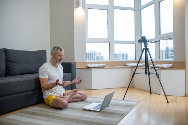 Yoga online. A mature man in white tshirt doing yoga tutorial online