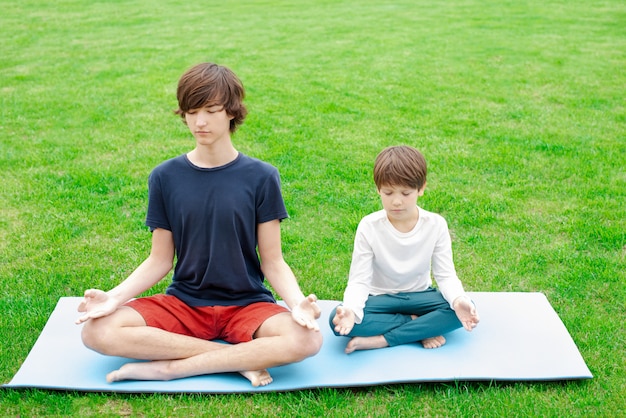 Yoga outdoor. Children sit in a lotus position on the green grass. Copy space.