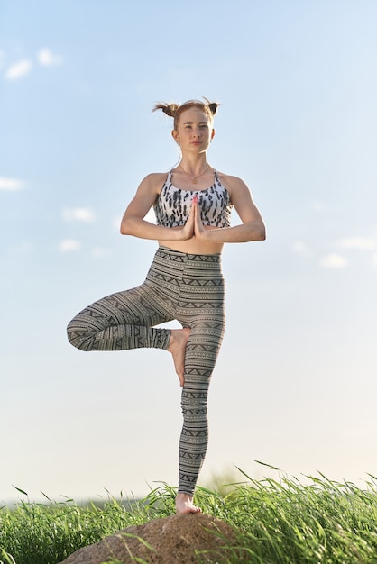 Йога на открытом воздухе. Счастливая женщина делает упражнения йоги, медитировать в солнечном парке. Концепция здорового образа жизни и отдыха. Красивая женщина практикующих йогу на траве