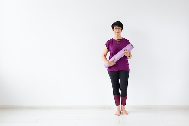 Yoga, people concept - Portrait of a middle age woman after yoga with her mat on white background