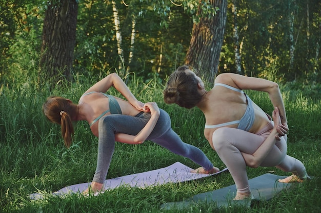 Istruttore personale di yoga che insegna alla giovane donna niralamba parsvakonasana all'aperto