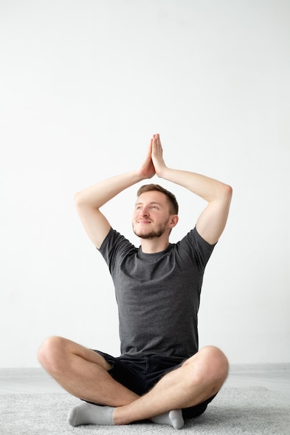 Foto pratica yoga ispirato uomo meditazione casa mente pacifica ragazzo sorridente calmo in pantaloncini maglietta seduta loto posa namaste mani in alto muro luce sfondo interno