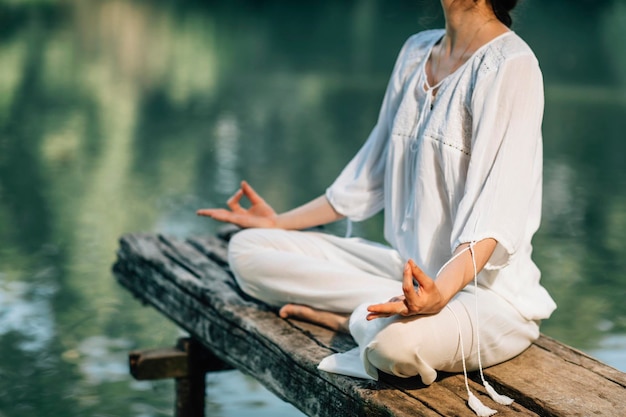 Photo yoga retreat peaceful young woman sitting in lotus position and meditating by the lake