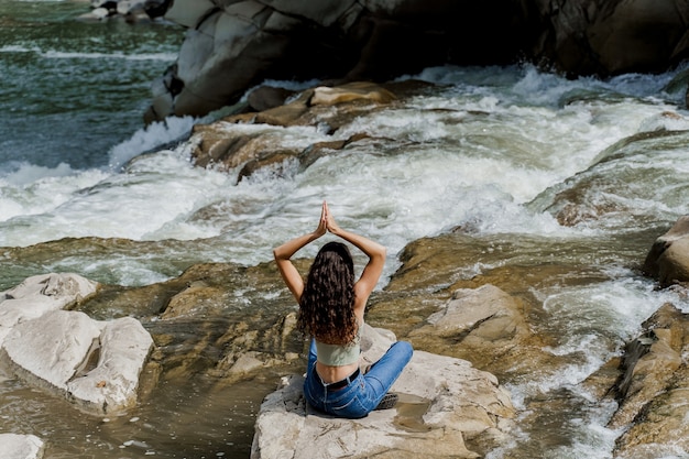 Yoga on the rocks near waterfall in mountain river. Girl travelling in Karpathian mountains.