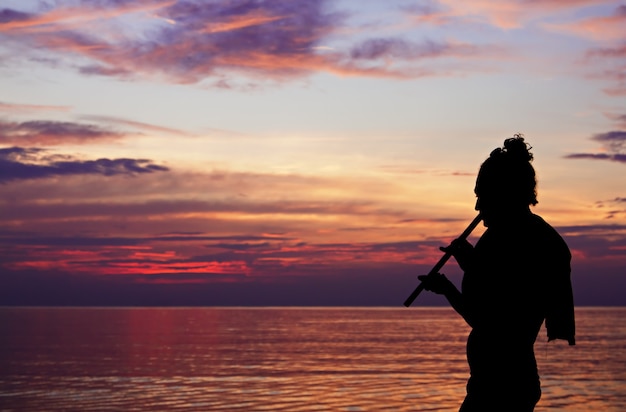 Yoga silhouette playing fluite at the sunset