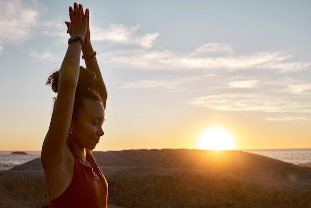 Foto yoga tramonto e natura con donna nera in spiaggia per la meditazione esercizio zen e mani di preghiera per la calma e la pace fitness donna all'aperto per allenamento per uno stile di vita sano energia e consapevolezza