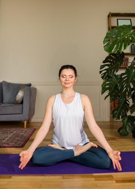 Yoga woman sits with her eyes closed in a lotus position on a rug in a room