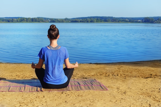 Yoga woman sitting on the river bank and meditating