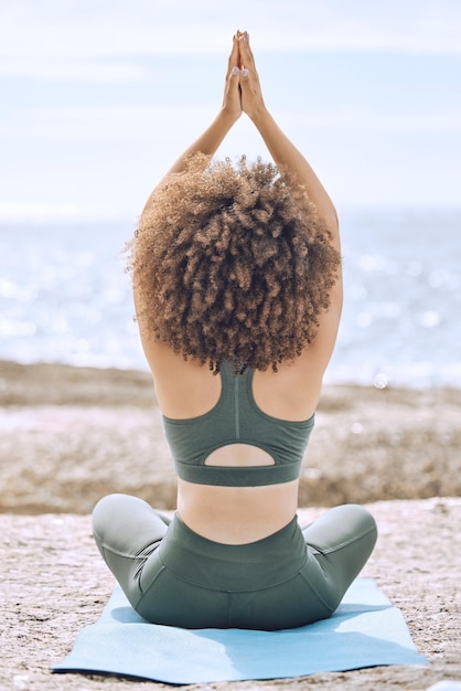 Yoga zen en achteraanzicht van zwarte vrouw op het strand op yogamat buitenshuis voor gezondheid, wellness of mobiliteit Meditatie handen omhoog gebedshouding of vrouwelijke training in pilates voor lichaamsbeweging, fitness of training