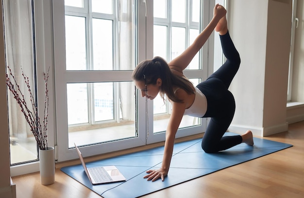 Yogalessen online Positief yogameisje dat ochtendoefening voor laptop thuis doet