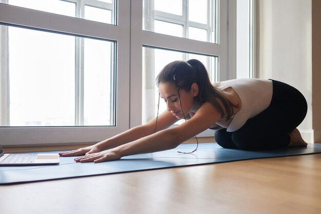 Yogalessen online Positief yogameisje dat ochtendoefening voor laptop thuis doet