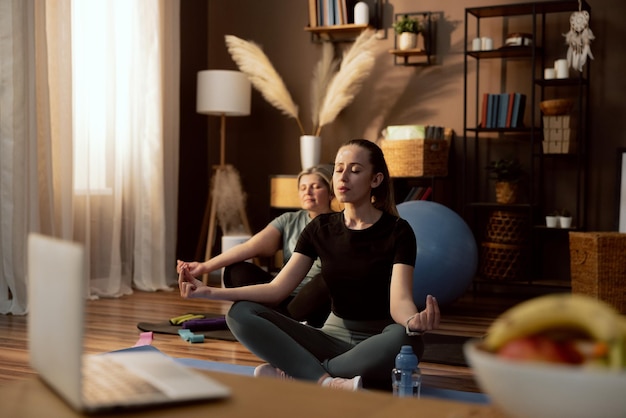 Yogatijd in moderne kamer jong meisje zittend op yogamat in lotos pose ogen sluiten ontspannend