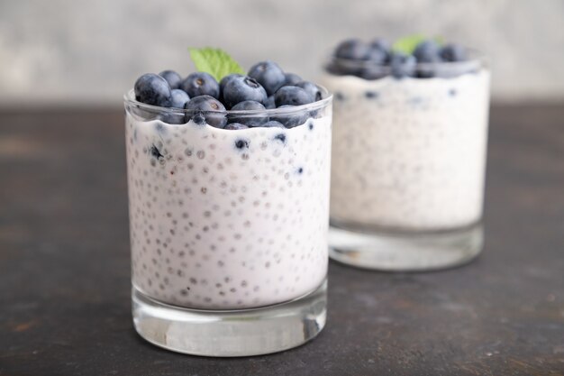 Yoghurt met bosbessen en chia in glas op zwarte concrete achtergrond. Zijaanzicht, close-up.