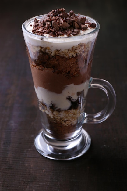 Yoghurt met chocoladeroom, gehakte chocolade en muesli geserveerd in glas op houten achtergrond