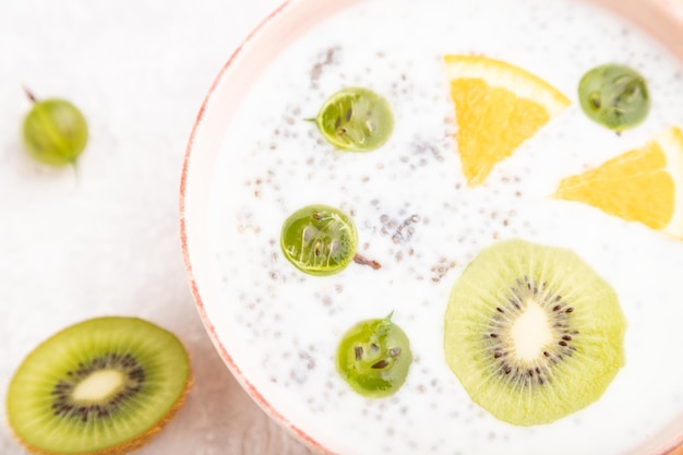 Yoghurt met kiwi, kruisbes, chia in keramische kom op grijze betonnen ondergrond en oranje linnen textiel. Bovenaanzicht, close-up, selectieve aandacht.