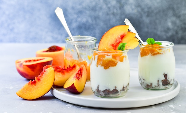 yoghurt met perzik jam en verse perziken in een ronde glazen pot op een grijze achtergrond, dessert recept. gezond ontbijt