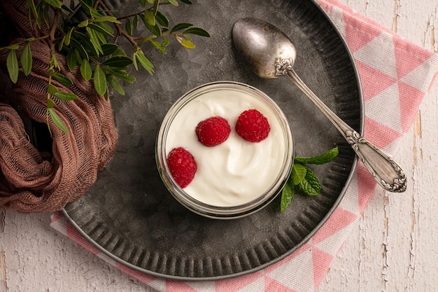 Yoghurt with raspberries on a metal plate on a white wooden table