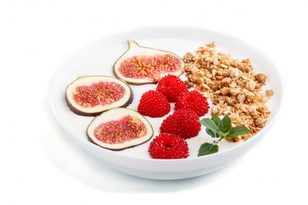 Yoghurt with raspberry, granola and figs in white plate isolated on white background. side view.