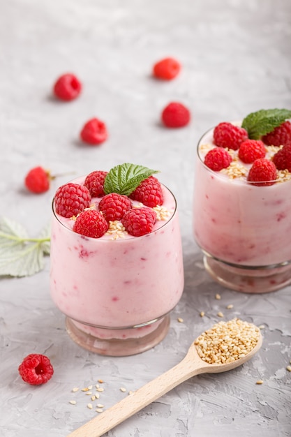 Yoghurt with raspberry and sesame in a glass and wooden spoon on gray concrete background. side view.