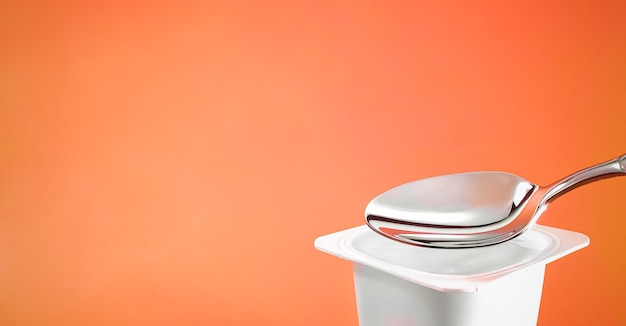 Yoghurtkop en zilveren lepel op oranje witte plastic container als achtergrond met yoghurtroom vers zuivelproduct voor gezonde voeding en voedingsbalans nutrition