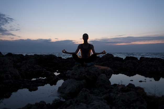 Yogi meisje in lotus houding op de rotsen in de buurt van de zee 's nachts