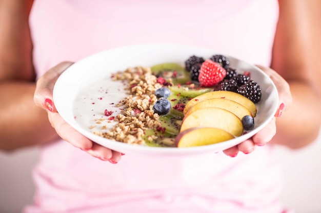 Yogurt blackberry muesli raspberries blueberries kiwi and peaches in a bowl holding young woman