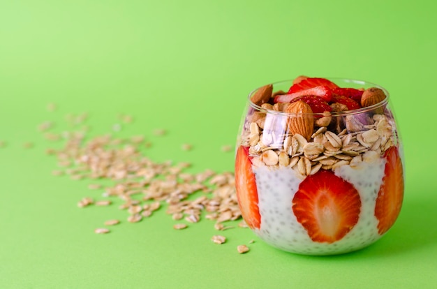 Yogurt chia pudding with fresh strawberries, oats and nuts in a glass on green 