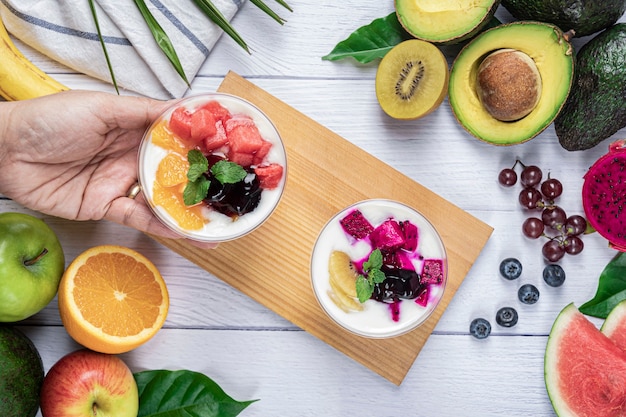 Yogurt and fruits on topping in a glass with a variety of fruit on the white wooden table wallpaper, Fruits. Healthy diet eating.