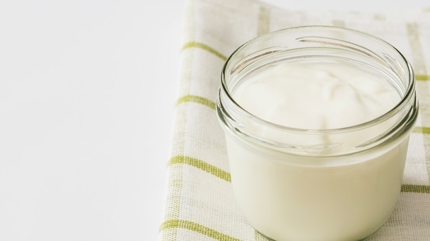 Yogurt in glass jar on napkin over the white backdrop