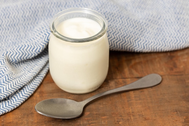 yogurt glass jar on wooden table with spoon and blue cloth still life
